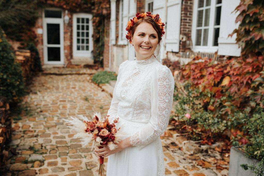 La mariée sourit avec son bouquet d'automne dans la cour du Domaine de Vaujoly