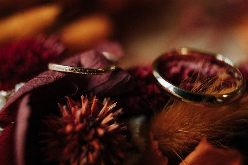 Alliances posées sur des fleurs séchées bordeaux et orangées, mariage d'automne au Domaine de Vaujoly