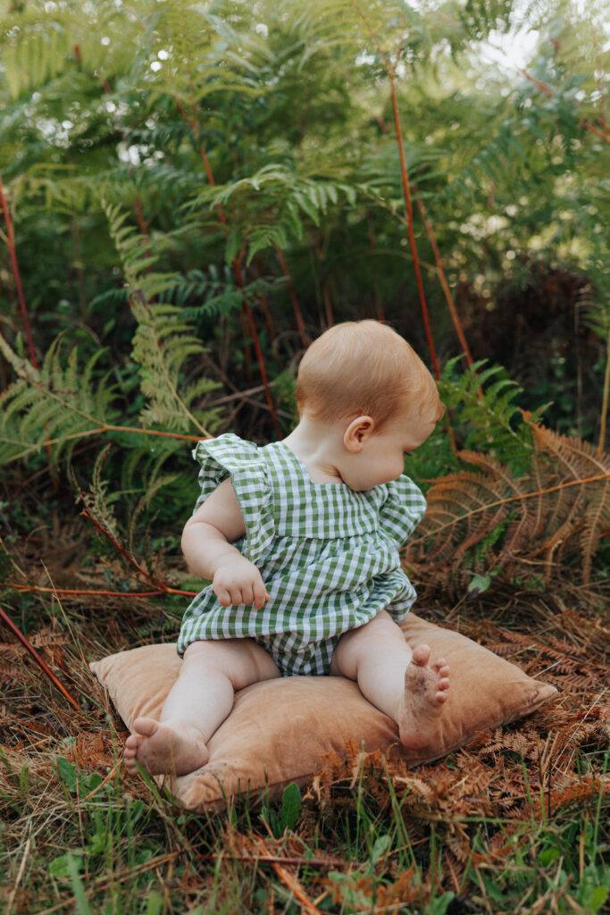 Bébé assis sur un coussin dans les fougères, séance photo famille en forêt