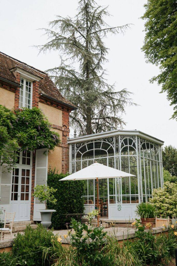Orangerie en verre et fer forgé du Manoir du Grand Courtoiseau entourée de verdure