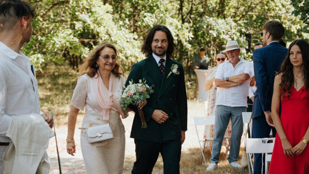 Entrée du marié en costume vert au bras de sa maman, cérémonie laïque au Domaine de la Volière