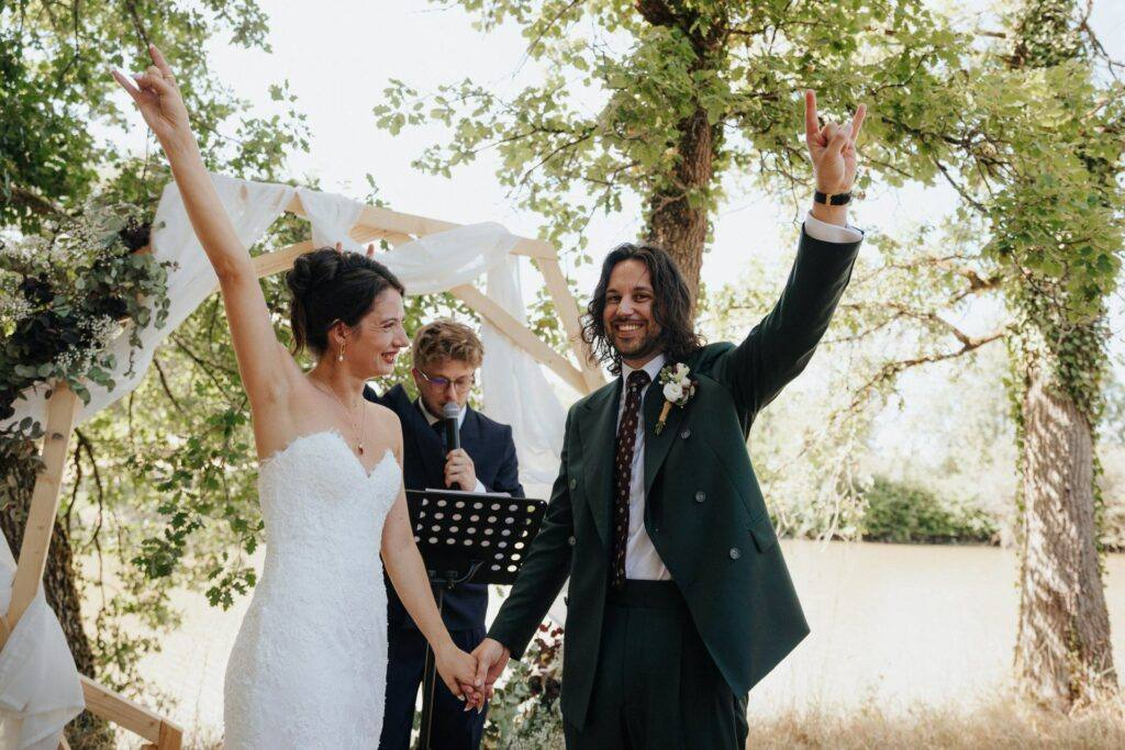 Les mariés lèvent les bras et font les cornes du rock devant l'arche de cérémonie au Domaine de la Volière
