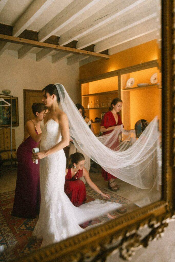 Les demoiselles d'honneur en rouge posent le voile de la mariée devant un grand miroir doré, Domaine de la Volière