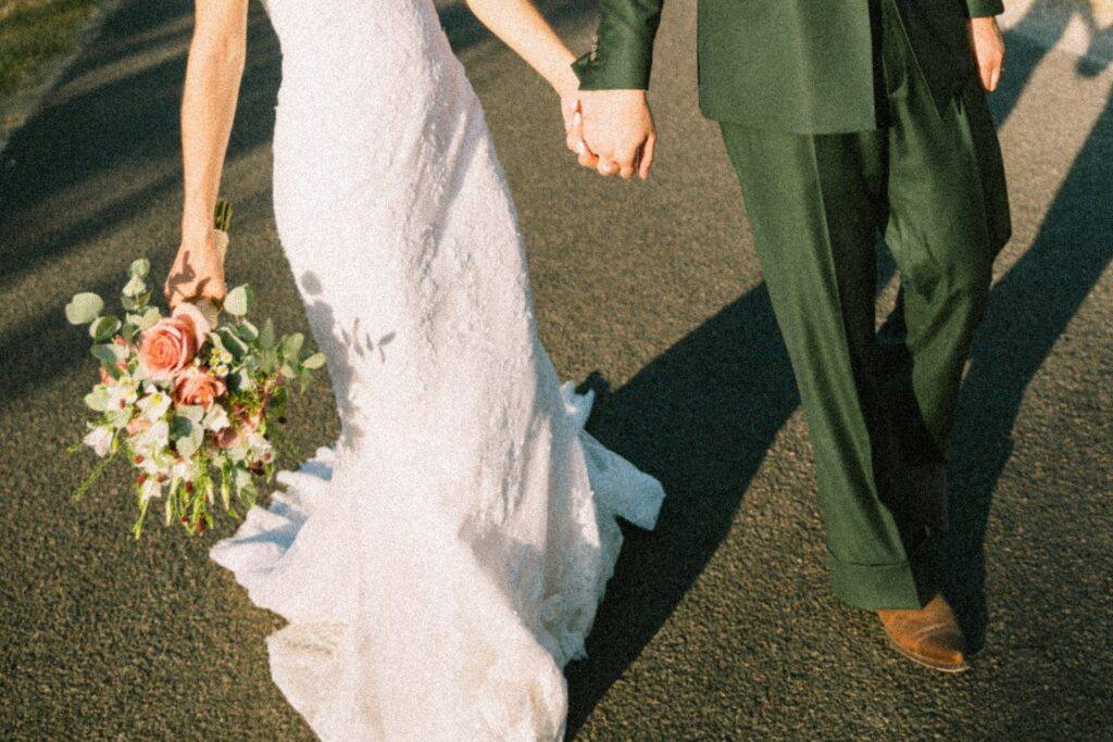 Mains entrelacées, bouquet de roses et costume vert, détail de la séance couple au Domaine de la Volière