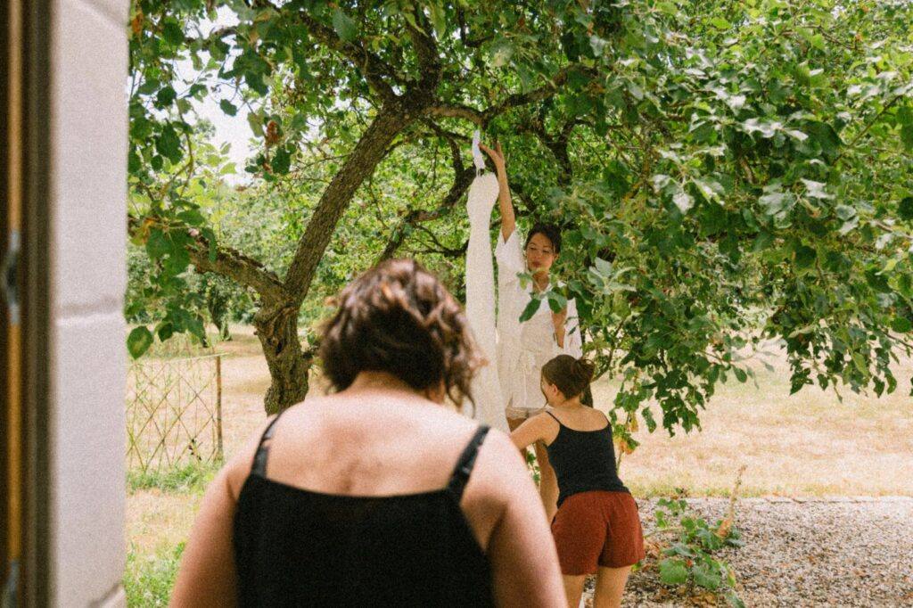 Robe de mariée en dentelle suspendue dans un arbre devant une bâtisse en pierre du Domaine de la Volière