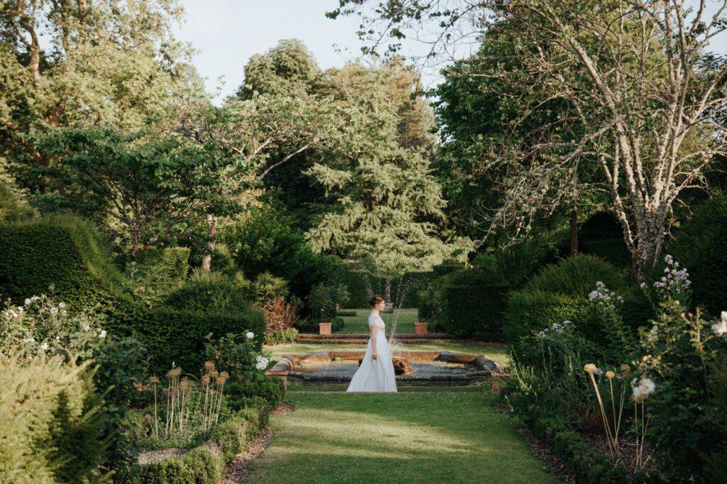 La mariée marche près de la fontaine du jardin à la française du Manoir du Grand Courtoiseau
