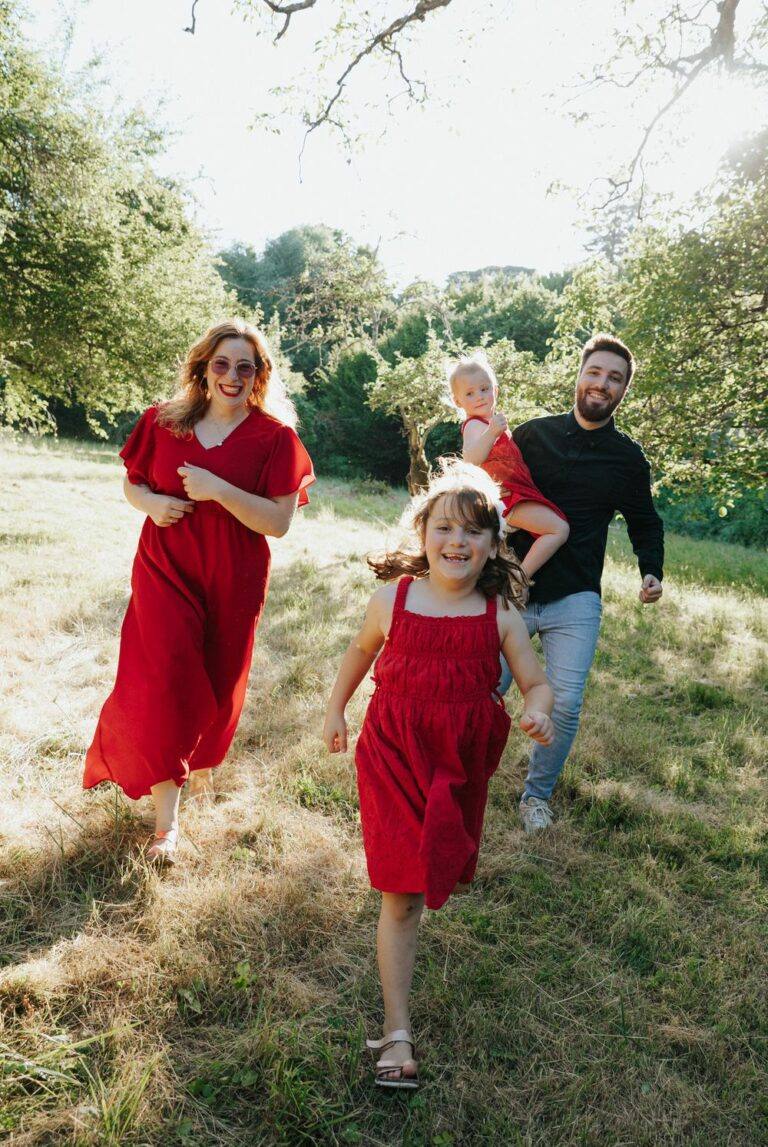 Famille en tenues rouges courant dans un pré ensoleillé lors d'une séance photo famille près d'Orléans, photographe Clara Valette