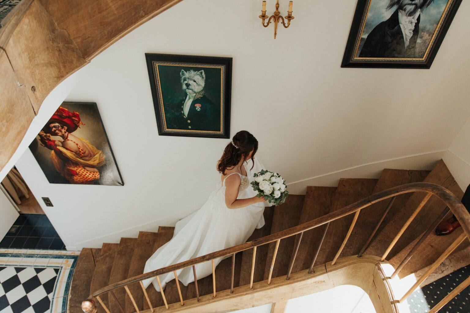 Mariée descendant l'escalier en bois avec son bouquet de pivoines au Château de la Vaudère, photographe de mariage Clara Valette
